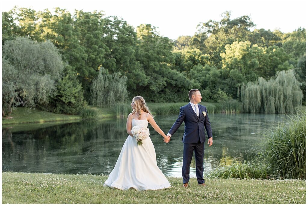 bride and groom holding hands by pond and looking in opposite directions at sunset at ironspire complex