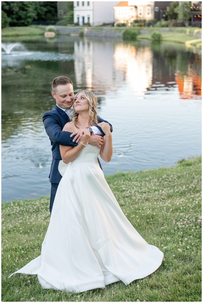 groom hugging his bride from behind as she leans back to kiss him by pond at ironspire complex