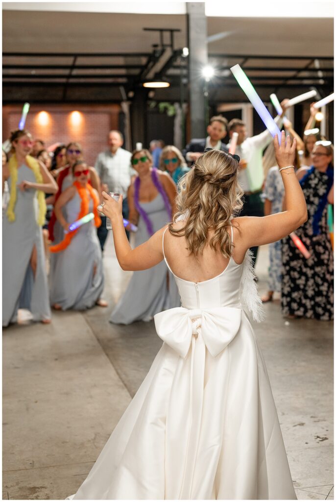 bride and her bridesmaids in light blue gowns raising large colorful glowsticks in the air during reception at ironspire complex