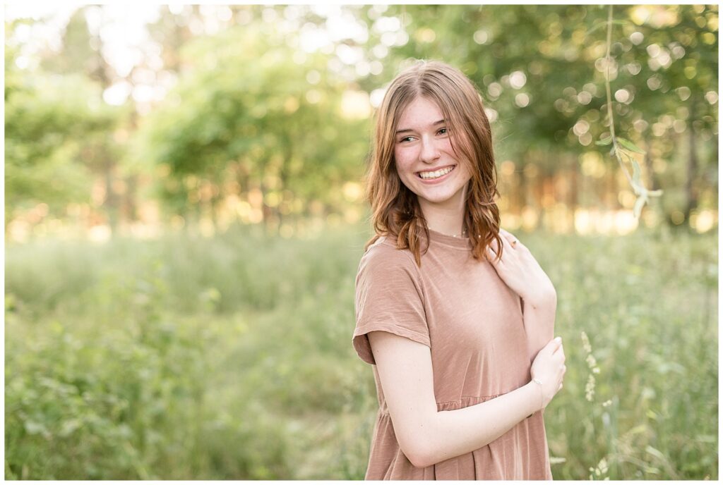 class of 2024 senior girl in light brown dress standing by tall wild grasses at overlook park