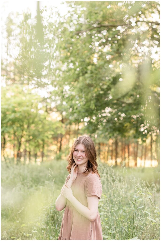 senior girl standing in wild grasses at sunset with right hand resting on jawline at overlook park