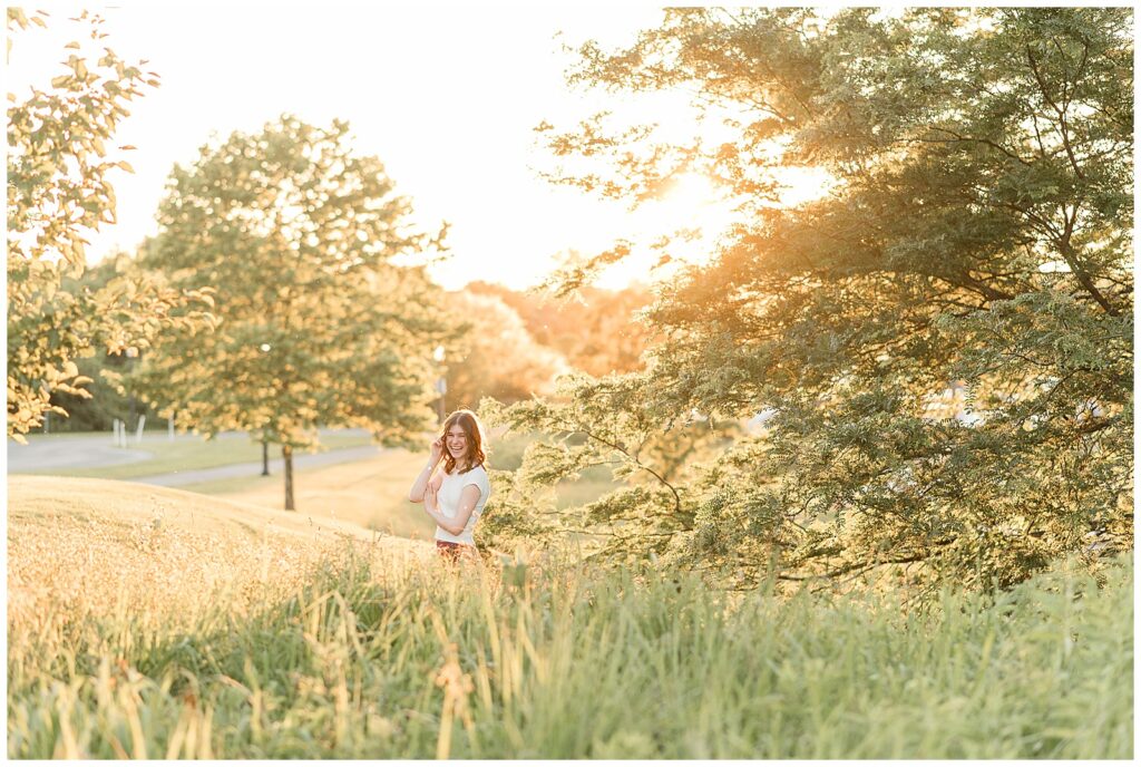 senior girl standing behind tall wild grasses with right hand in her hair at sunset at overlook park