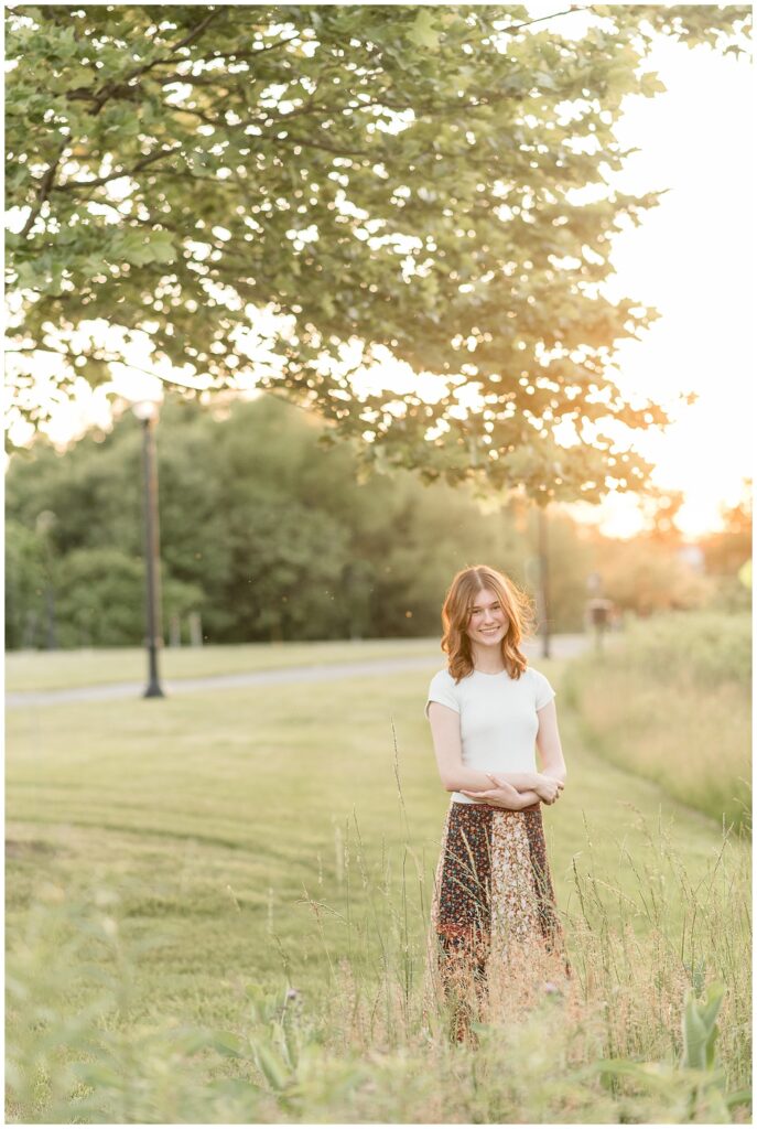 senior girl standing in grass with arms folded in front of her at overlook park in lancaster pa