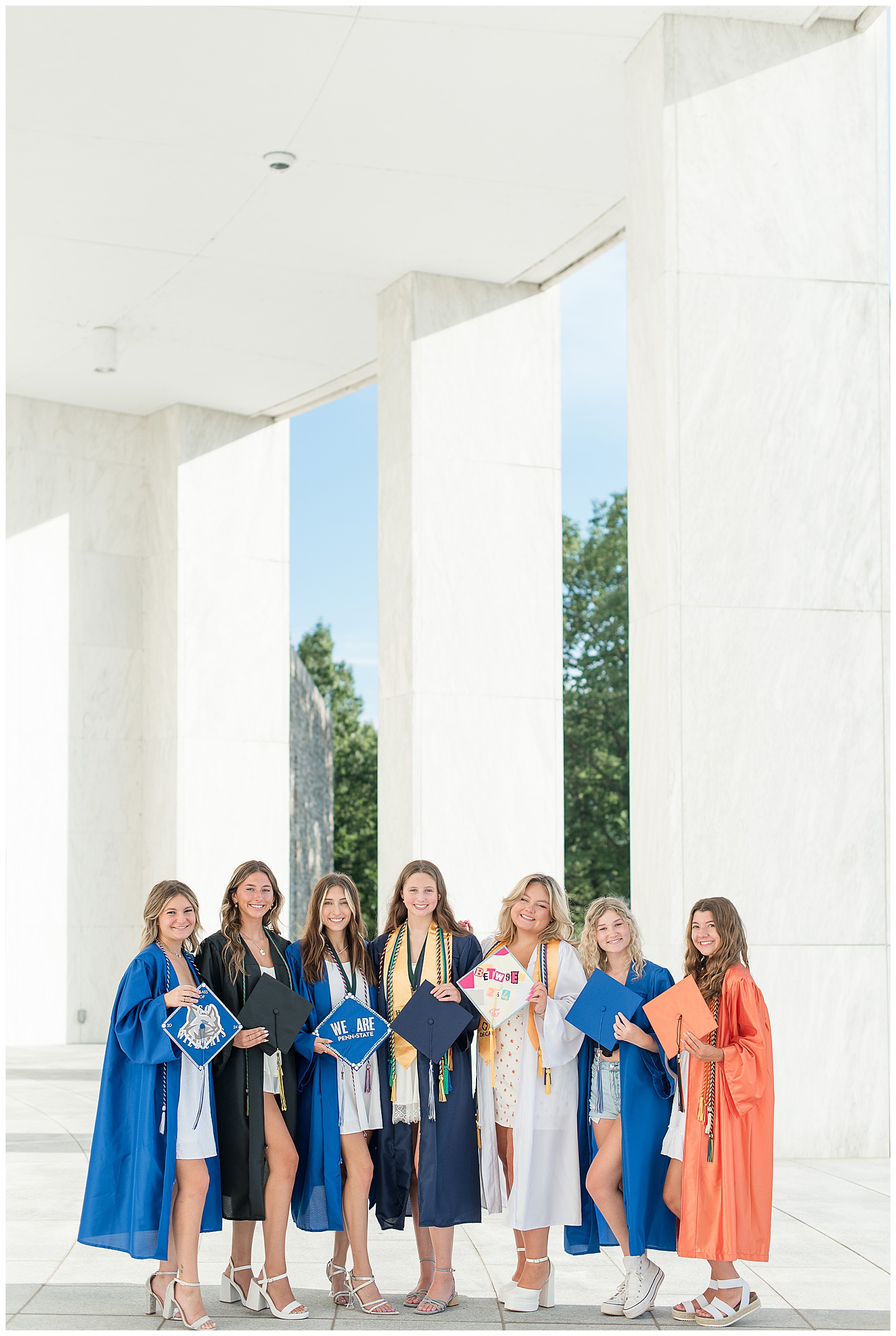 seven senior girls wearing their graduation gowns and holding their caps at founders hall in hershey pennsylvania