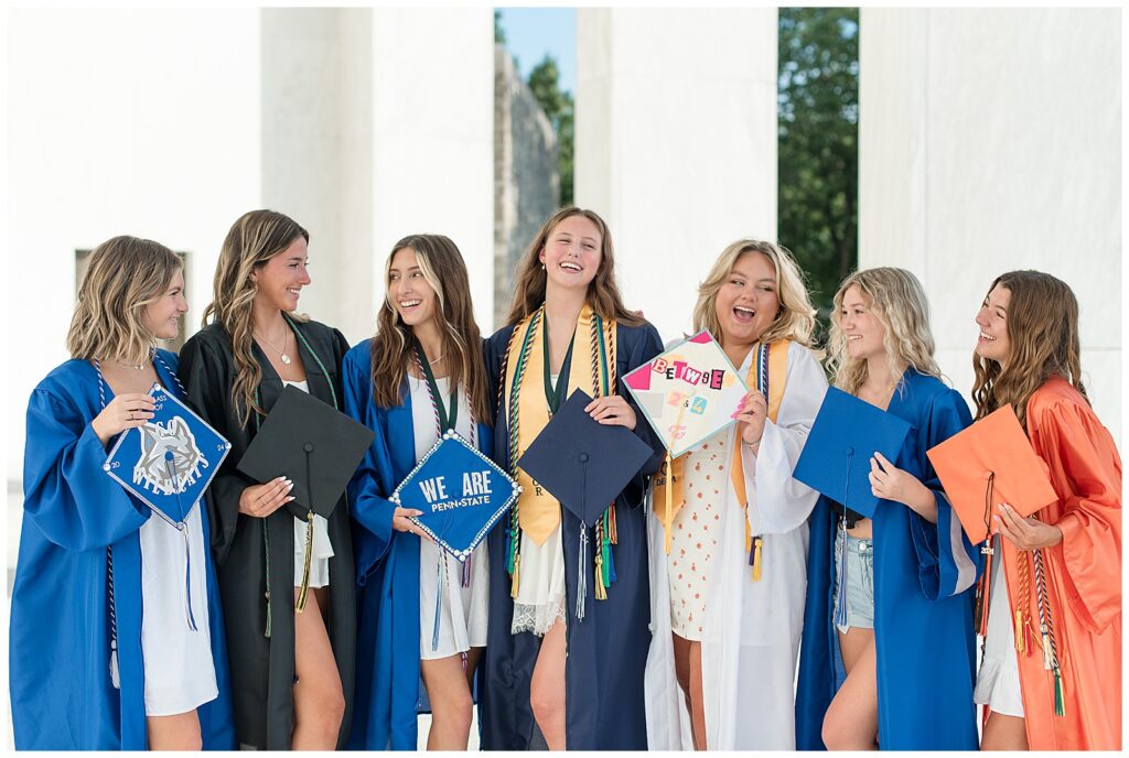 senior girls in colorful graduation gowns holding caps and all smiling at each other at founders hall in hershey pa