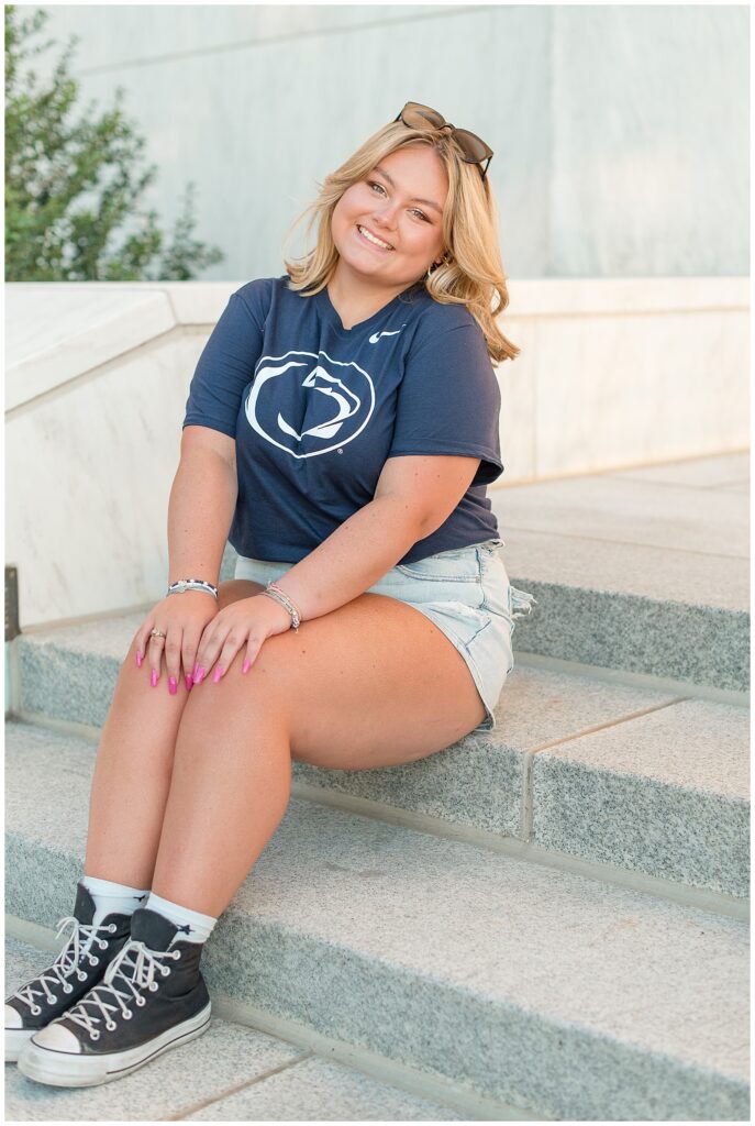 senior girl sitting on steps with hands on her knees wearing penn state t-shirt and shorts at founder's hall in hershey pennsylvania