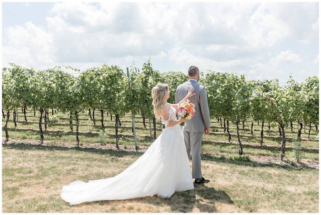 bride behind groom tapping him on his back for first look moment in vineyard at folino estate