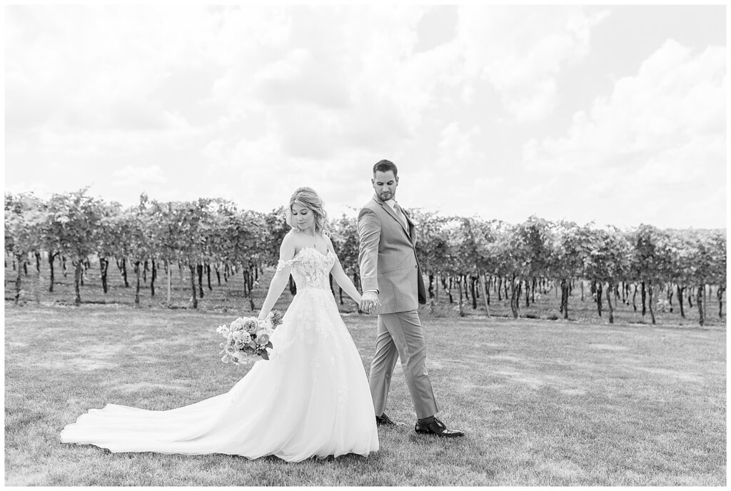 black and white photo of couple holding hands and walking looking back over their right shoulders at folino estate winery