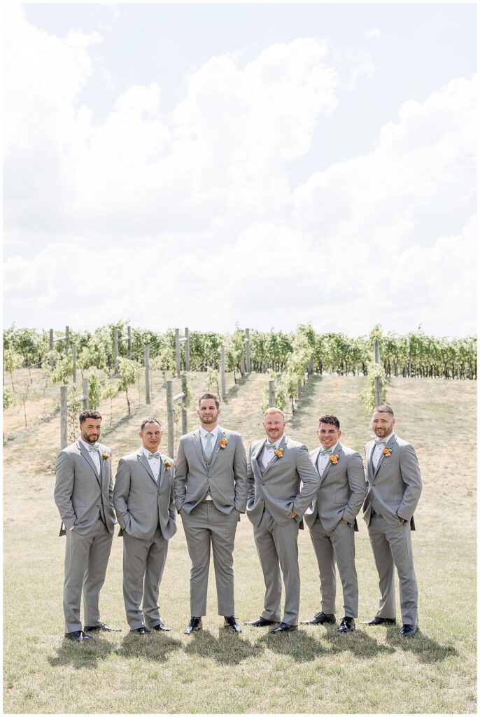 groom with his five groomsmen all wearing gray suits with hands in pockets at vineyard at folino estate