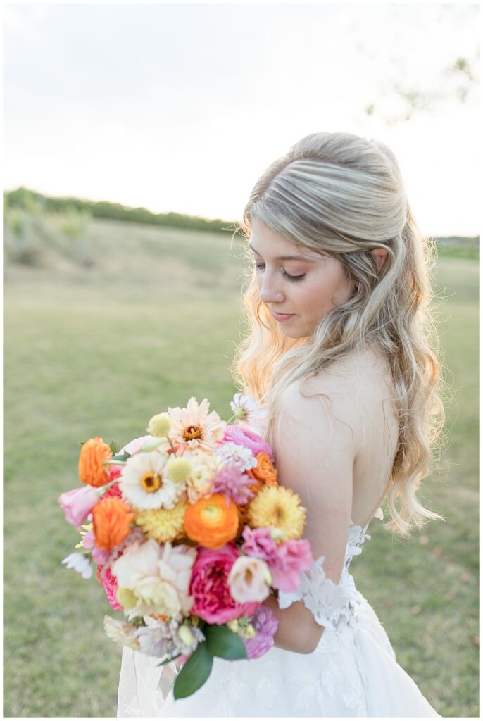 bride looking down at her colorful bouquet of flowers in vineyard at folino estate