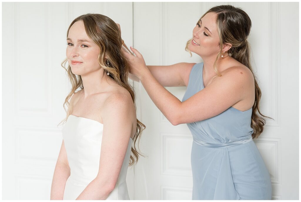 maid of honor smiling while placing the veil on the bride's head