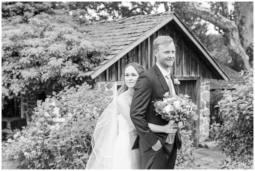 black and white photo of bride hugging groom from behind. Both looking in opposite directions 