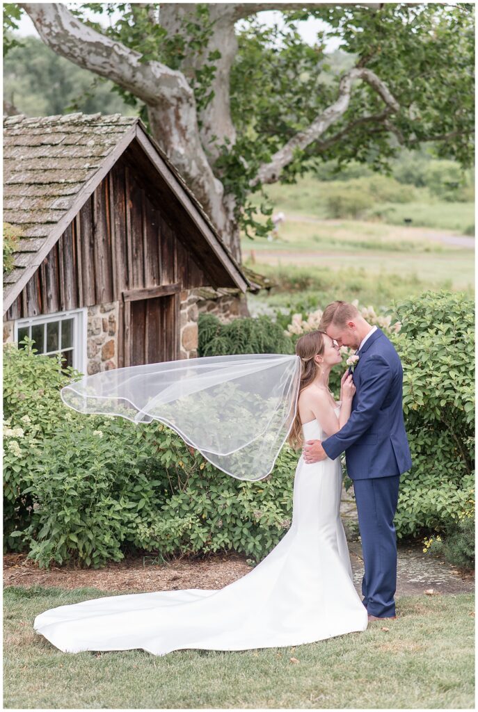 bride and groom portrait with veil flowing in the wind as bride and groom face towards each other and rest foreheads together