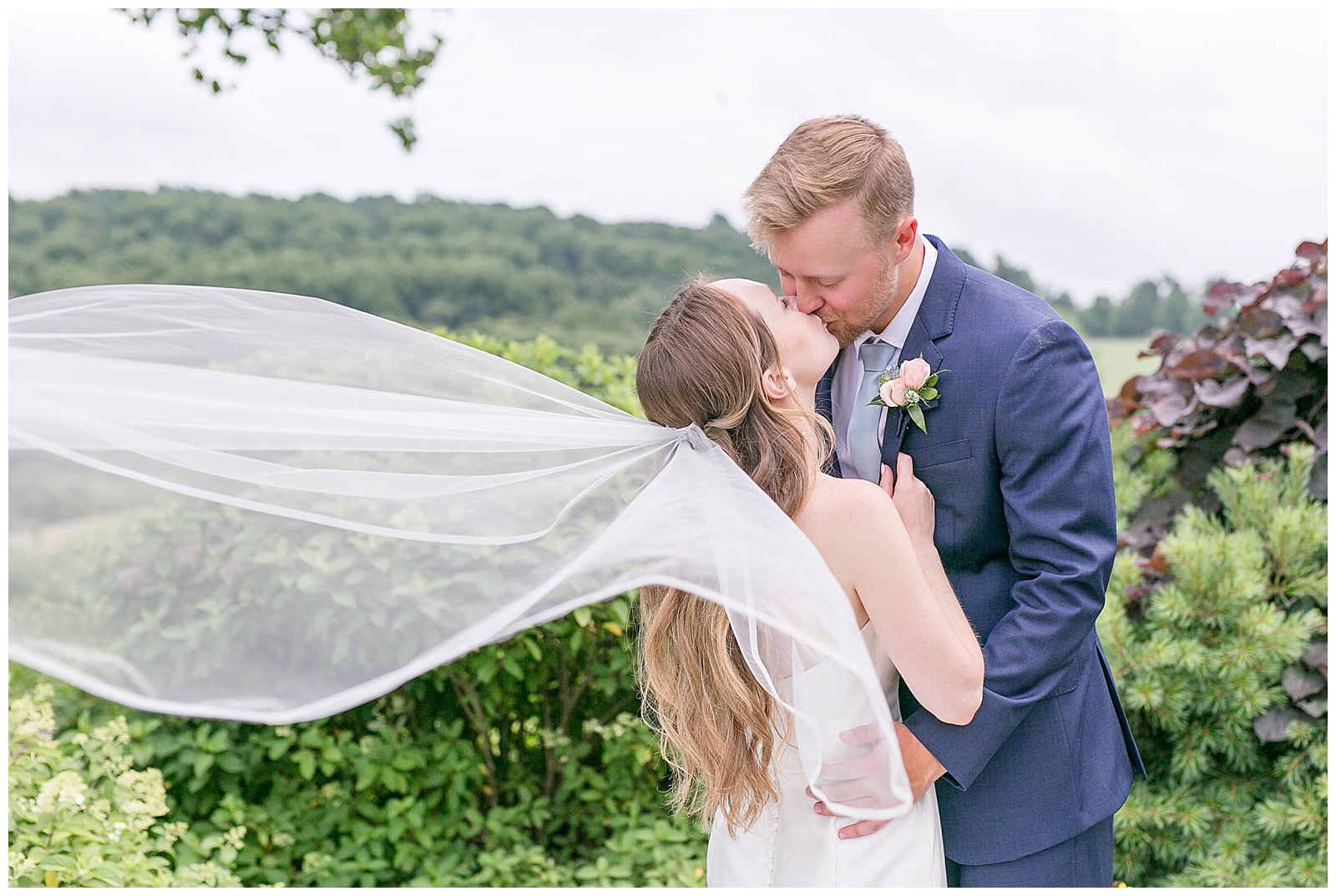 bride and groom portrait with veil flowing in the wind as bride and groom face towards each other and share a kiss