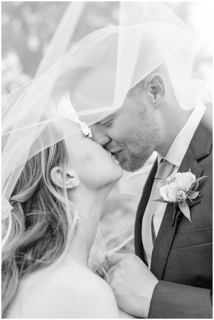 black and white photo of. bride and groom kissing under veil 