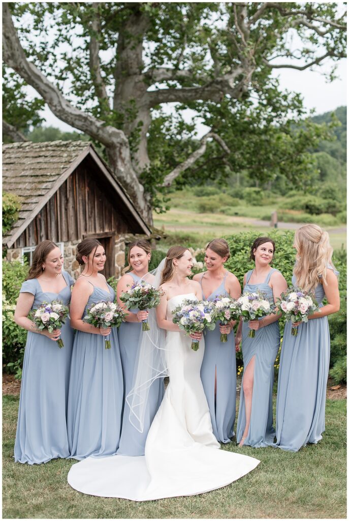 bridesmaids photo with girls all in light blue dresses holding bouquets with white and purple flowers smiling at each other