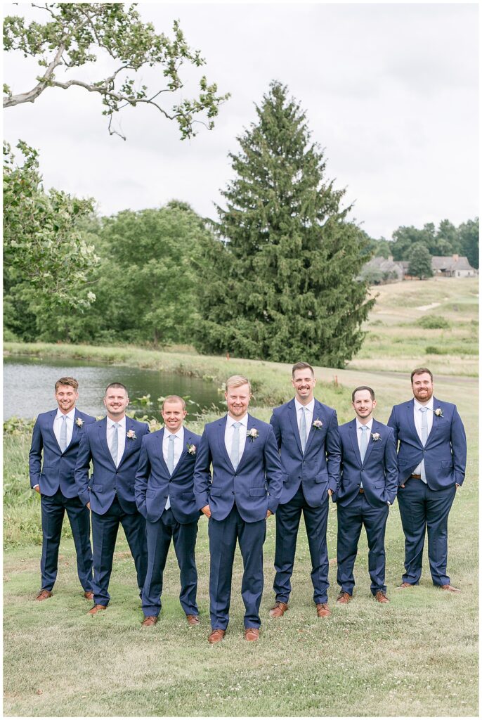 groomsmen shot of guys standing in triangle format smiling at camera with hands in pocket