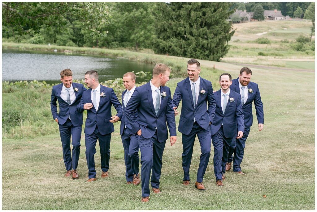 groomsmen in navy suits walking towards camera and talking together