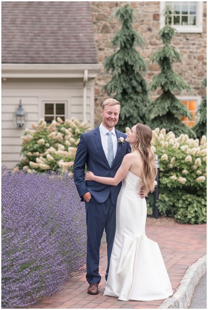 bride and groom sunset portraits beside lavender pushes as bride smiles up to groom and he smiles to camera