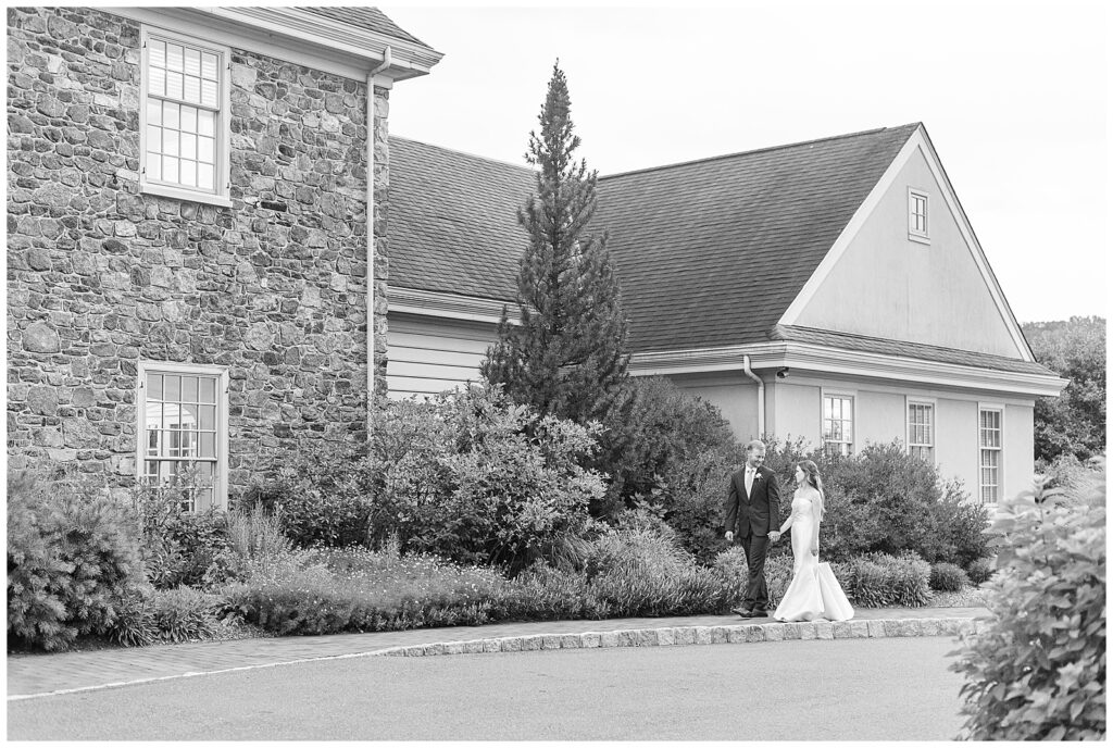 black and white photo of bride and groom holding hands walking along front walk of French Creek Golf Club