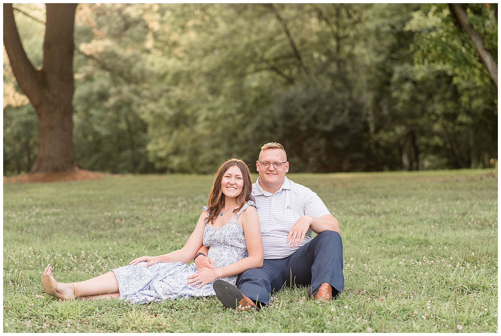 engaged couple sitting in the grass smiling with trees behind them at lancaster county central park