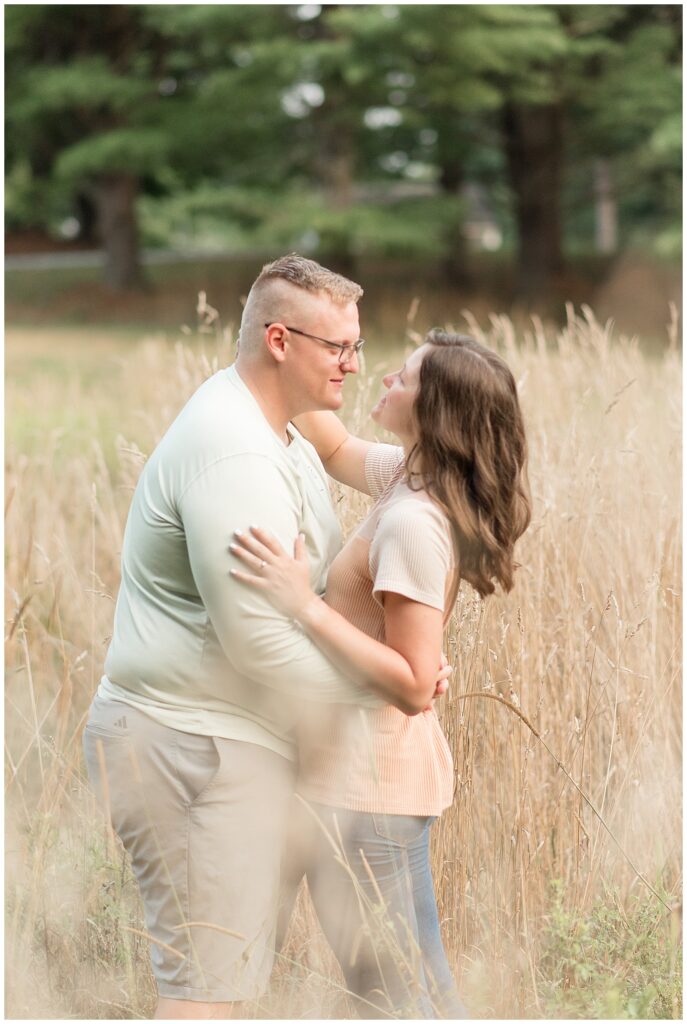 engaged couple hugging in field of tall, dry wild grasses as they get ready to kiss in lancaster county central park