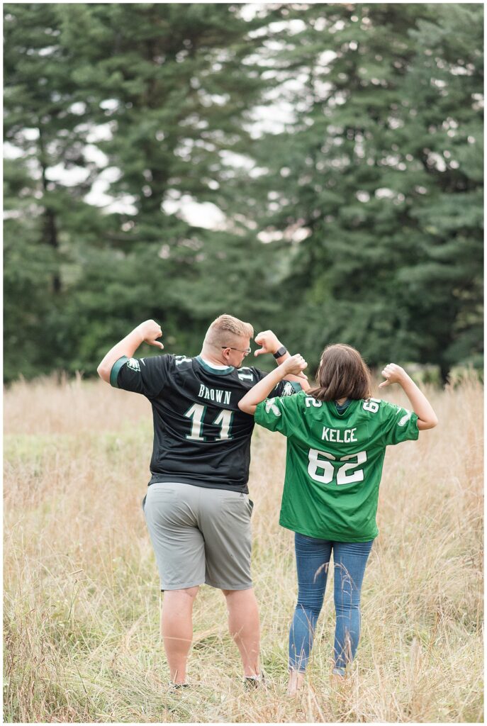 engaged couple with their backs toward the camera as they show off their football jerseys at lancaster county park