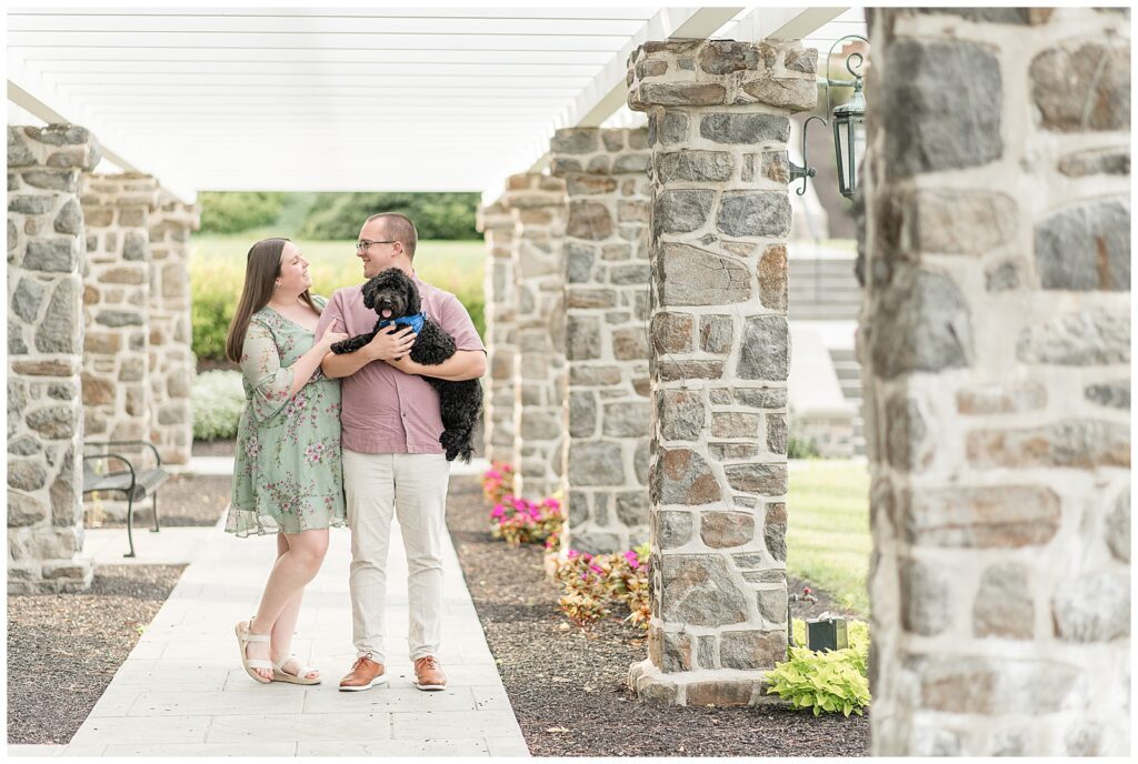 engaged couple holding their pup by stone columns at masonic village in elizabethtown pennsylvania