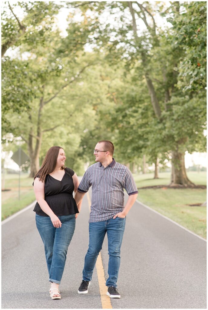 engaged couple holding hands and walking down middle of road at masonic village