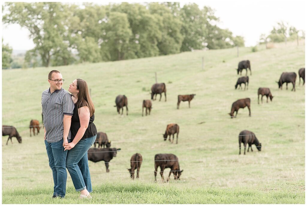 woman standing behind man as they hold hands by field of cows in elizabethtown pennsylvania