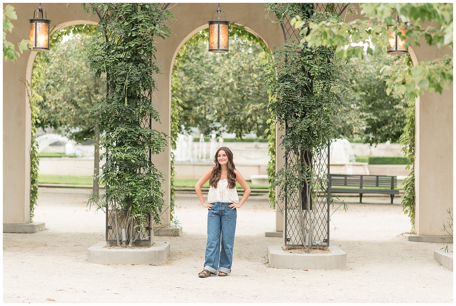 senior girl standing between concrete archway with hands on hips at longwood gardens in chester county pa