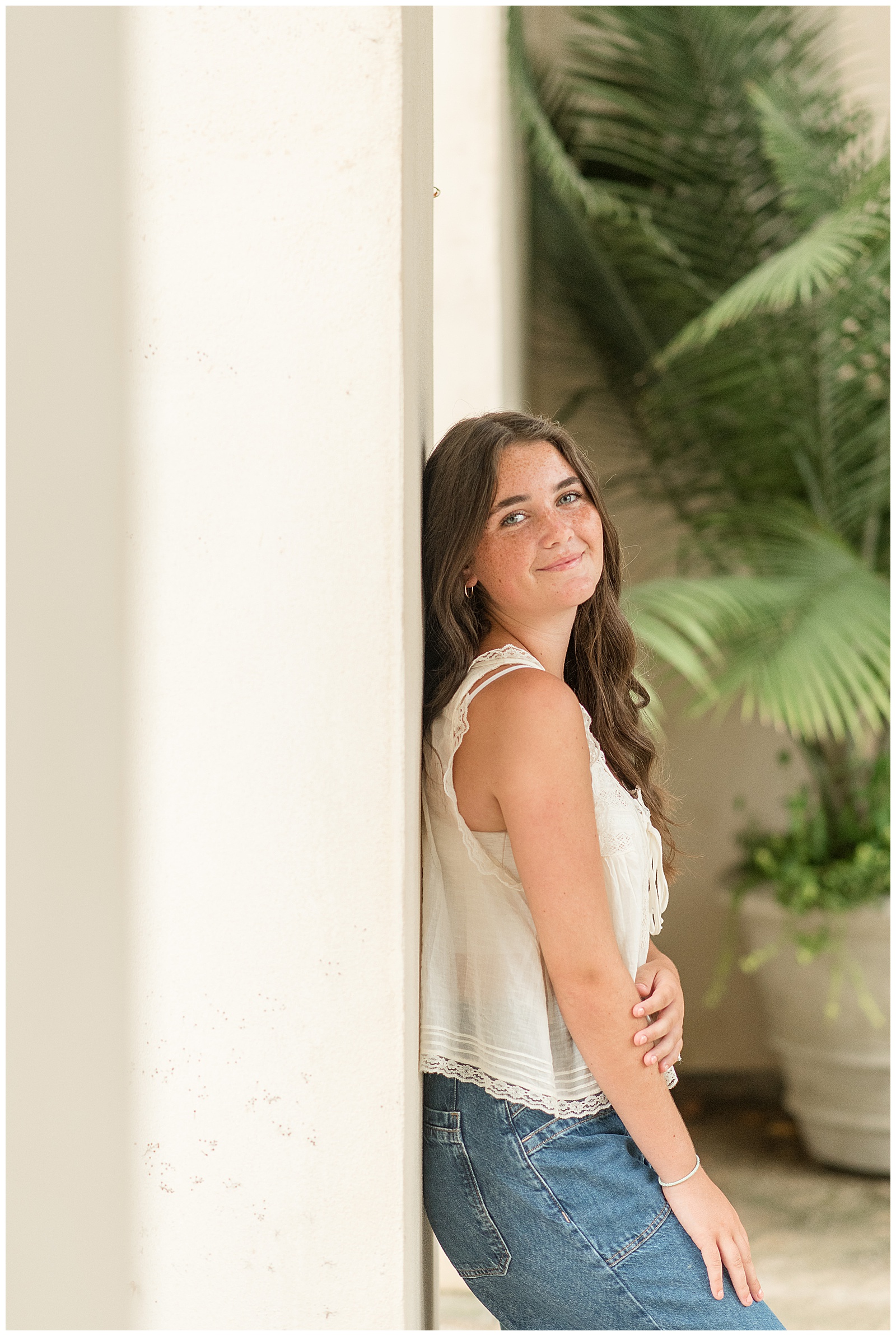 senior girl leaning against white concrete wall with right shoulder toward camera at longwood gardens