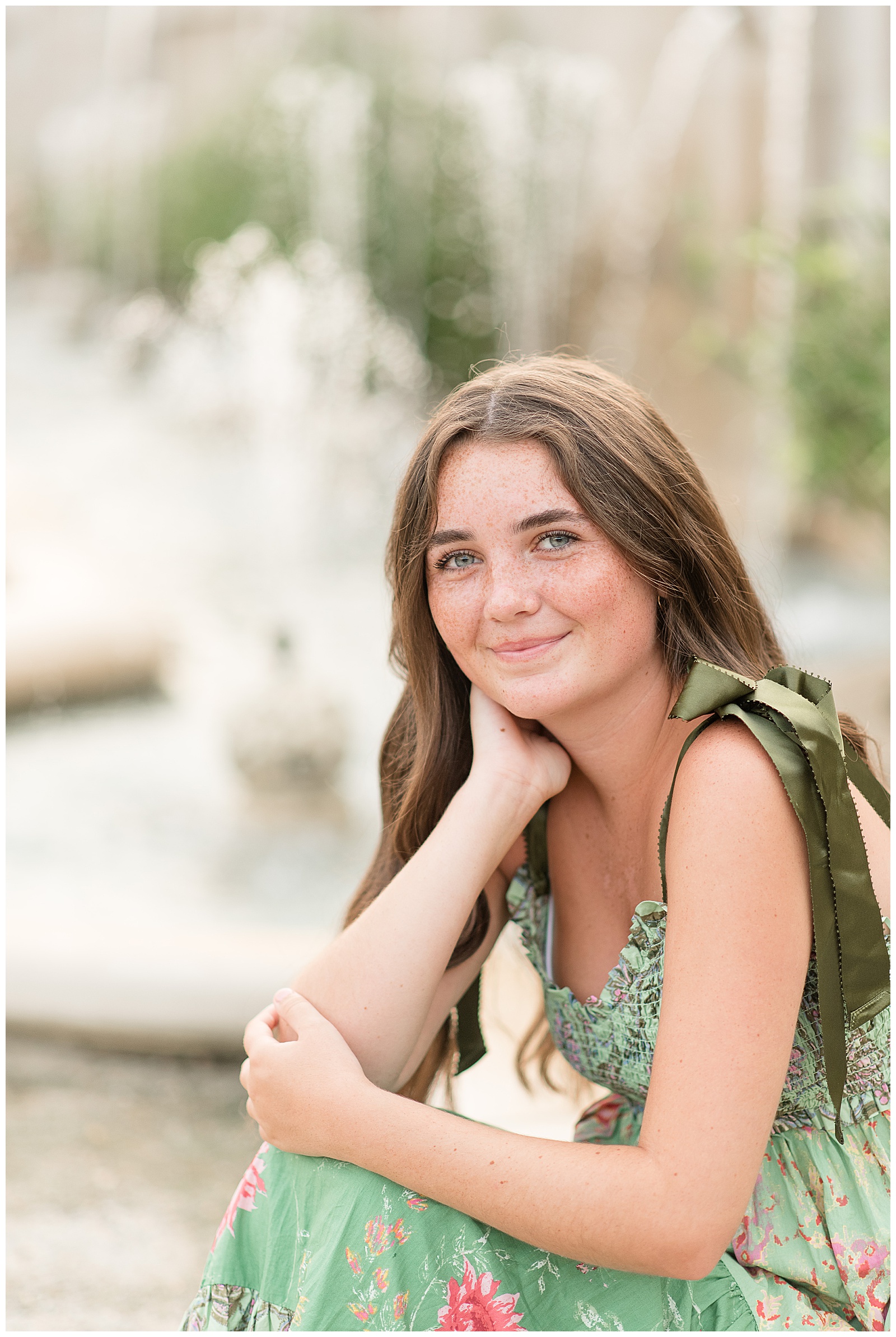 close up photo of senior girl sitting by fountains and resting her right hand against her neck at longwood gardens