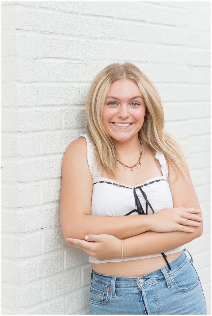 girl senior spokesmodel in white tank top and jeans leaning against white brick wall in lancaster pa