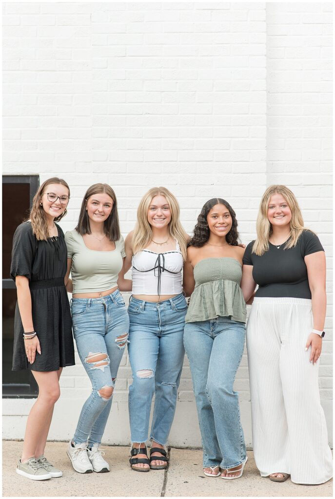 five senior girl spokesmodels in shades of sage green, white, black, and blue jeans by white brick wall in lancaster city