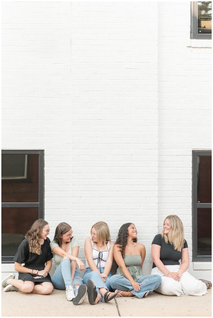 class of 2025 senior spokesmodels sitting on sidewalk by white brick building in downtown lancaster