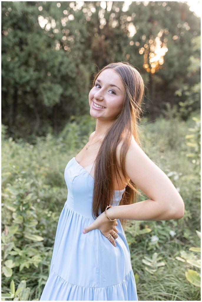 senior girl in light blue dress with hands on hips and left shoulder toward camera at overlook park