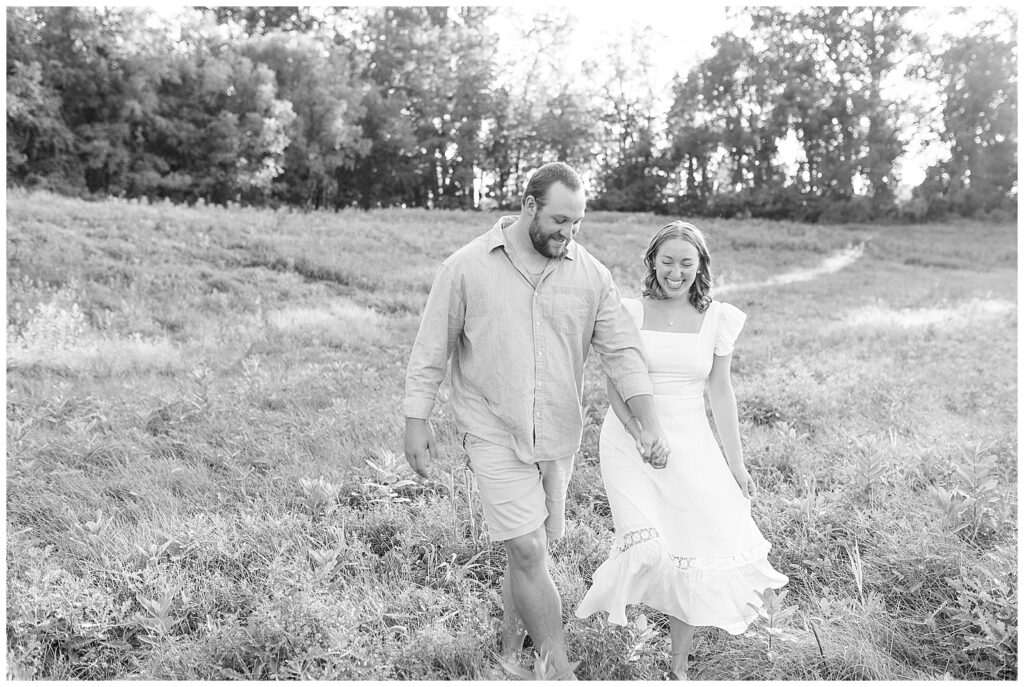 black and white photo of engaged couple walking in field at sunset at hibernia park in pennsylvania