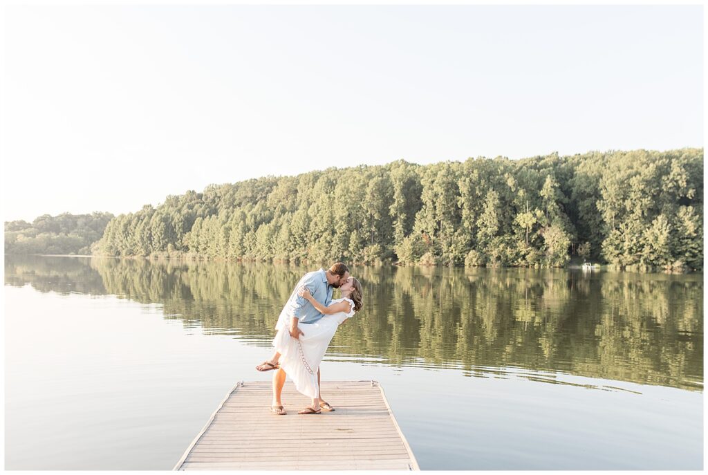 guy dipping back girl on wooden dock as they kiss with lake behind them at hibernia park