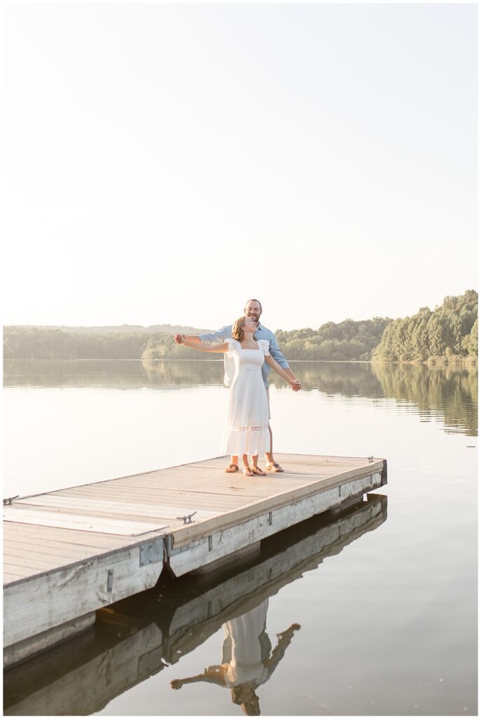 guy standing behind girl as the hold hands and extend them out on dock at hibernia park