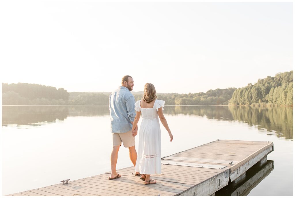 engaged couple walking on dock with backs toward camera at sunset at hibernia park in chester county pennsylvania