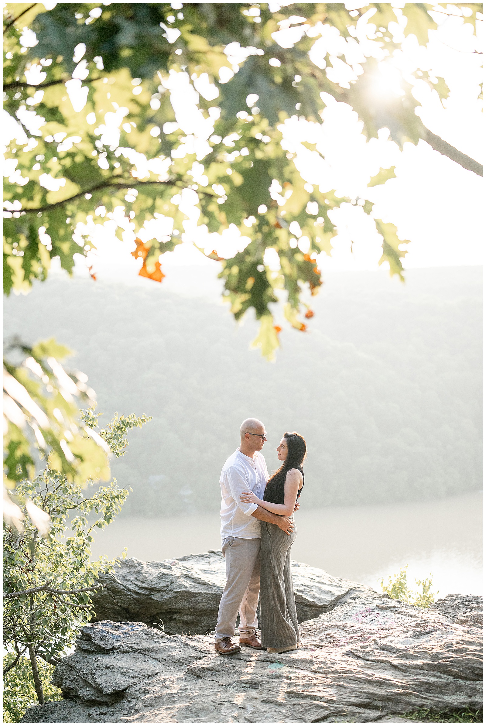 engaged couple hugging as they smile at each other on large rock by overlook at pinnacle point in lancaster pa