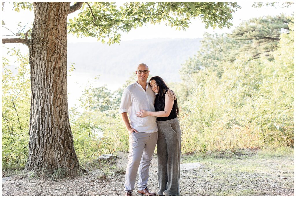 woman resting her right cheek on man's left shoulder by tree at pinnacle overlook