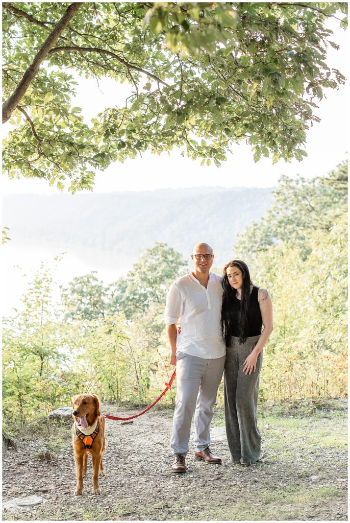 couple holding their dog's leash by trees with susquehanna river behind them at pinnacle point