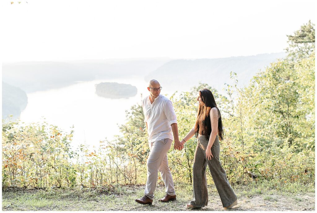 couple holding hands and walking along path with susquehanna river below and behind them