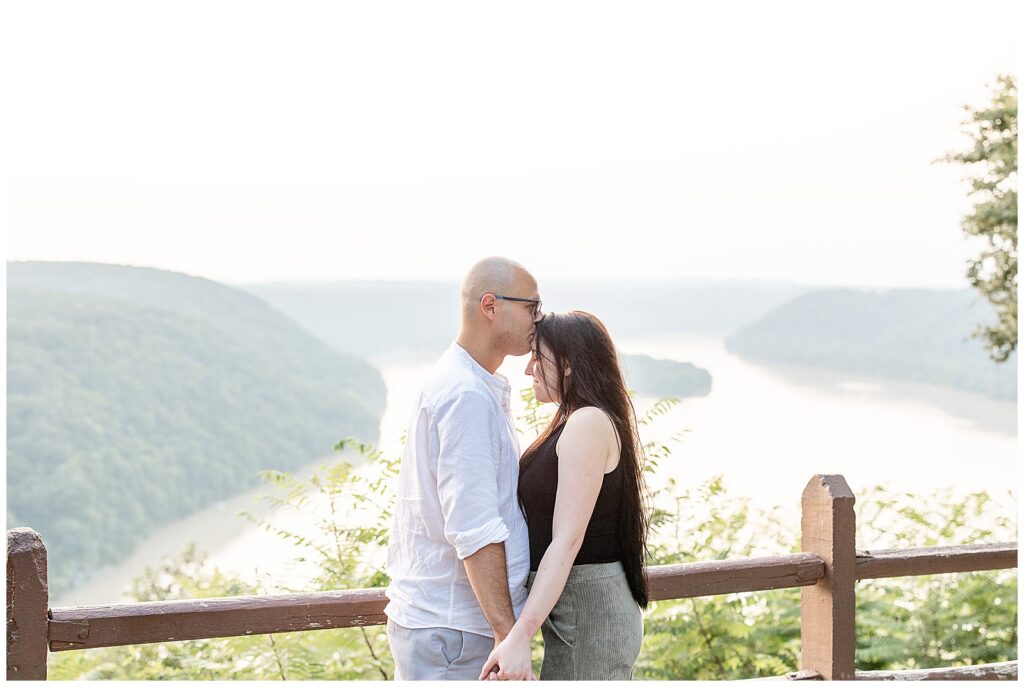 man kissing the top of woman's forehead as they hold hands at pinnacle point