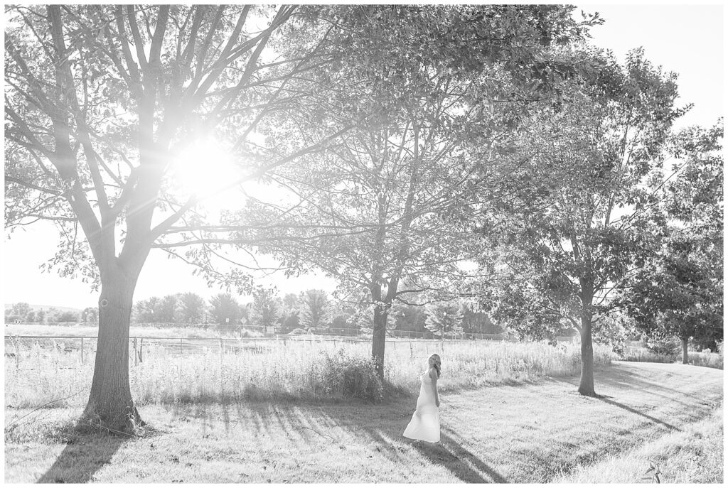 black and white photo of senior girl standing in grass by wildflower field at sunset at overlook park