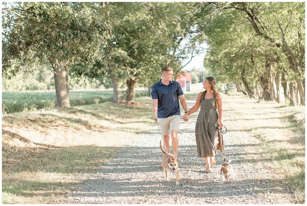 couple holding hands and their pups' leashes as they walk toward camera in chesapeake city maryland