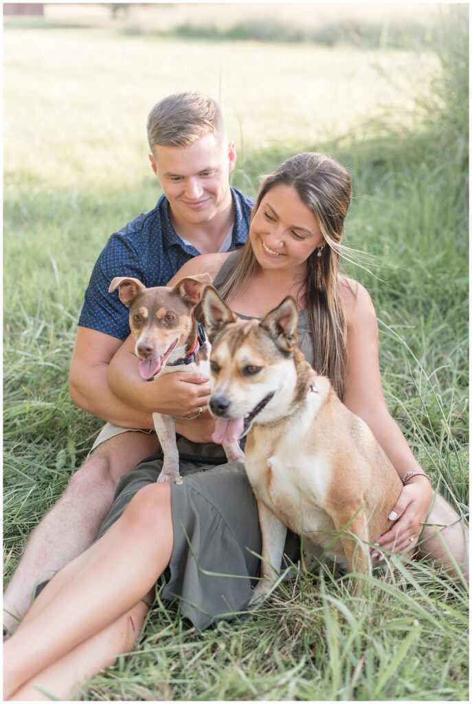 closeup photo of couple sitting in the grass with their two pups on their laps at family farm in maryland