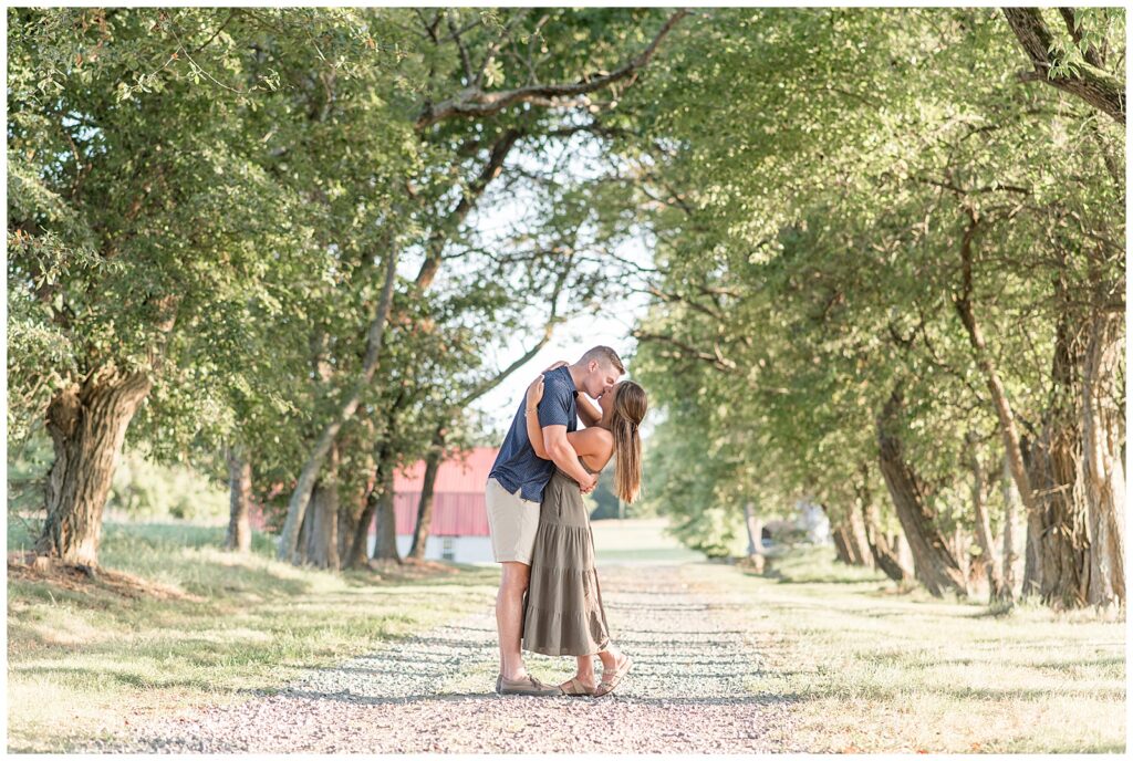 engaged couple kissing as guy slightly dips girl back on tree-lined path in maryland